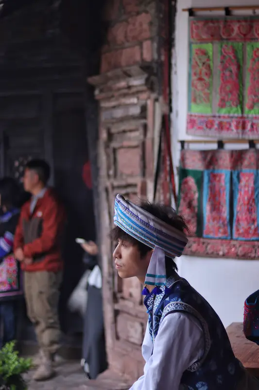 A Bai man in traditional white and blue Bai clothing looking into the distance.