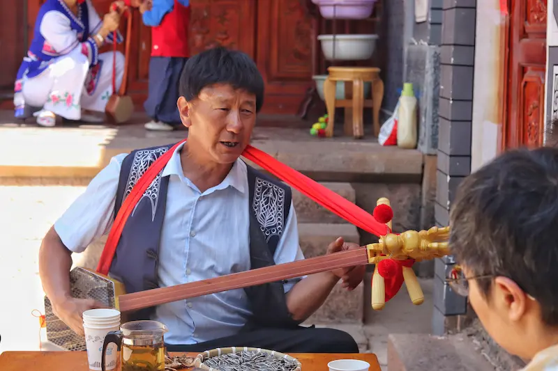 A Bai musician playing traditional Bai tunes for his guests on a three-stringed dragon-headed instrument.
