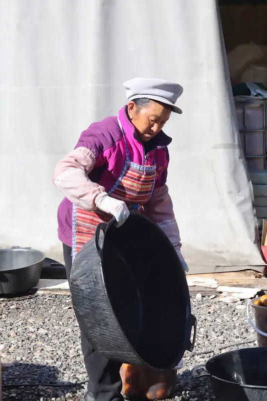 A Bai woman moving a large black plastic basin used for storing pears.