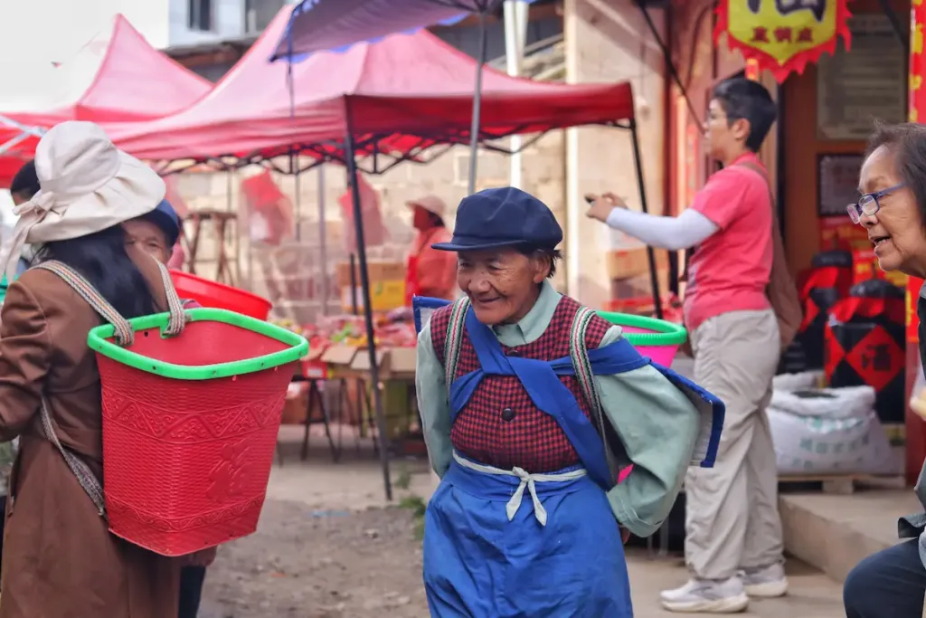 A Bai woman with a traditional back basket walking through an ethnic market.