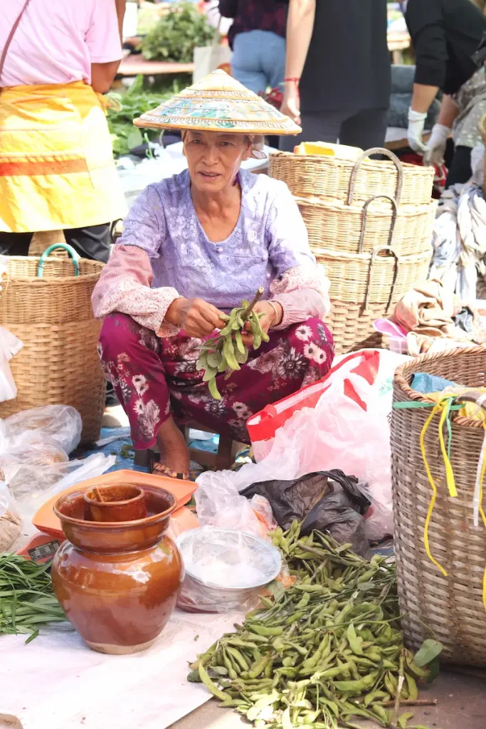 A Dai woman selling edamame while wearing a bamboo hat in Mangshi.