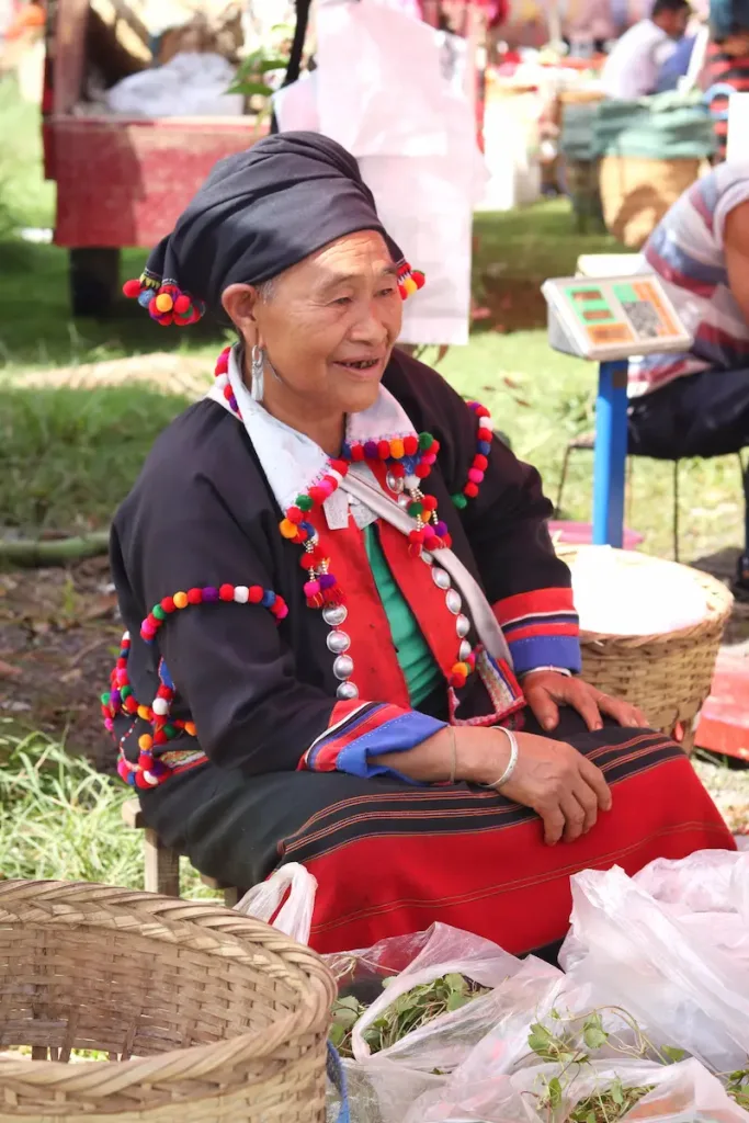 A De'ang woman selling goods and smiling at a local market in Mangshi.
