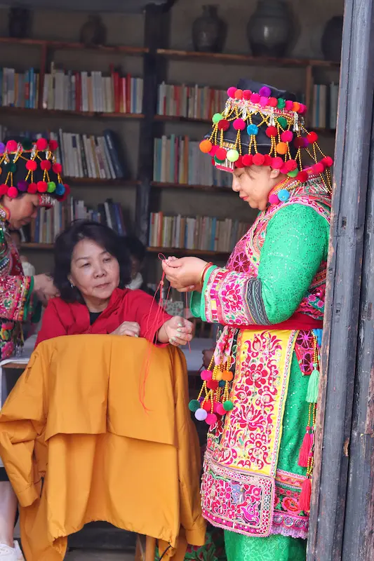 A Malaysian guest watching a Yi woman make a macramé bracelet.