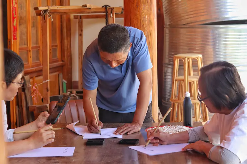 A Naxi Dongba master practicing Dongba pictographic script with two Singaporean guests.