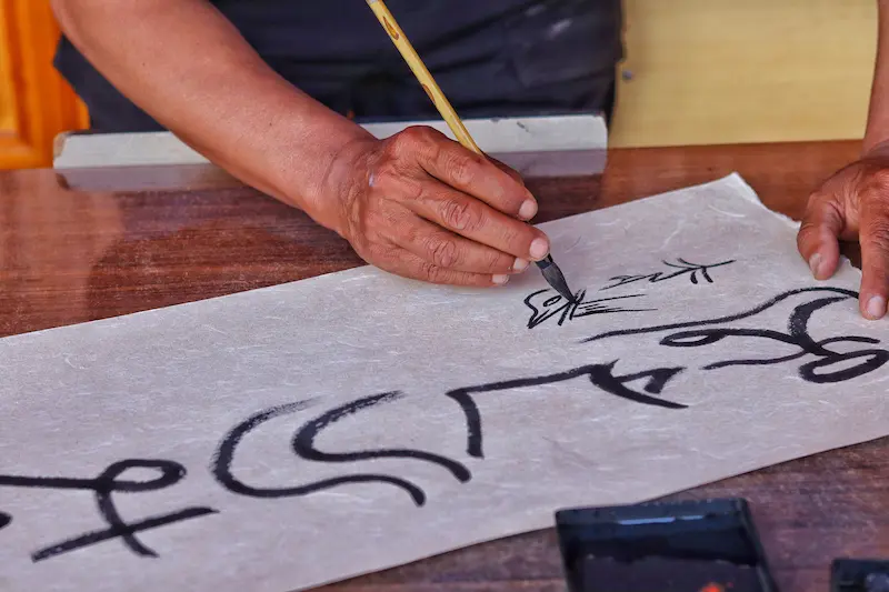 A Naxi Dongba master writing in Dongba pictographic script on traditional Dongba paper.