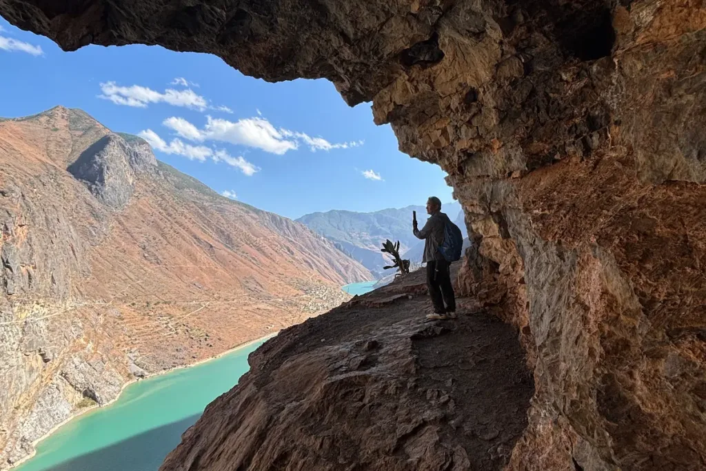 A Naxi village guide standing on a cliffside path with the blue Jinsha River below.