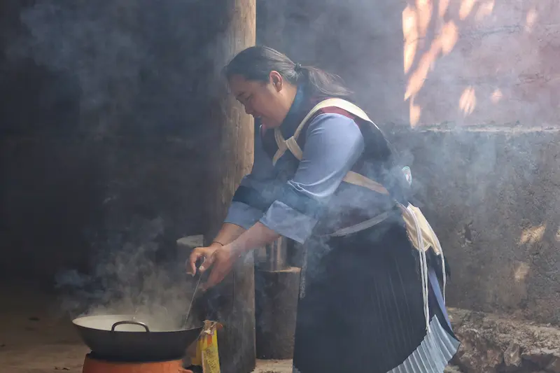A Naxi woman smiling and boiling Lijiang chicken pea juice.