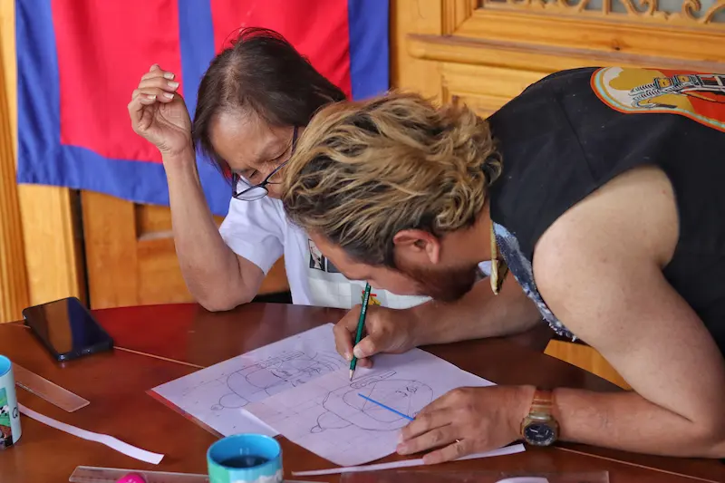 A Singaporean guest learning to draw a Thangka Buddha with a Tibetan artist.