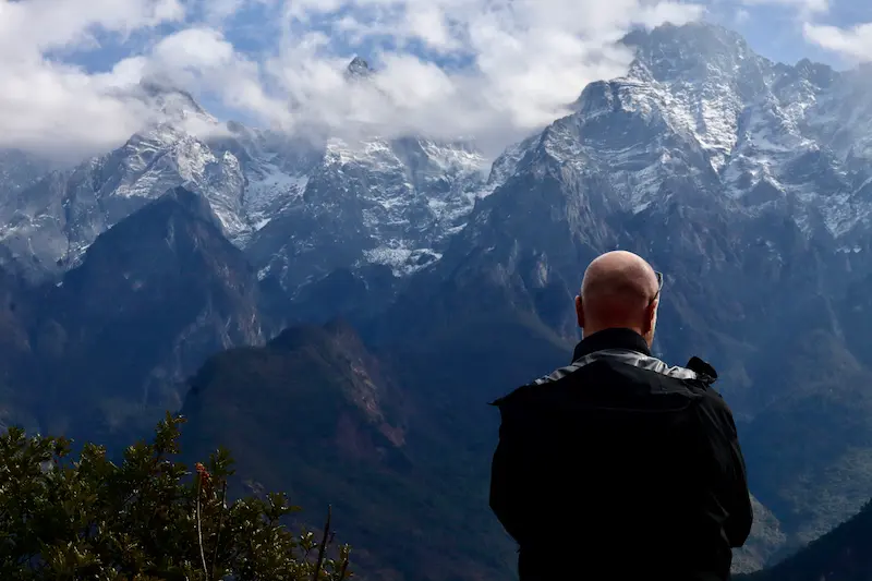 A Swedish guest standing with his back to the camera, with snow-capped mountain peaks in the background.