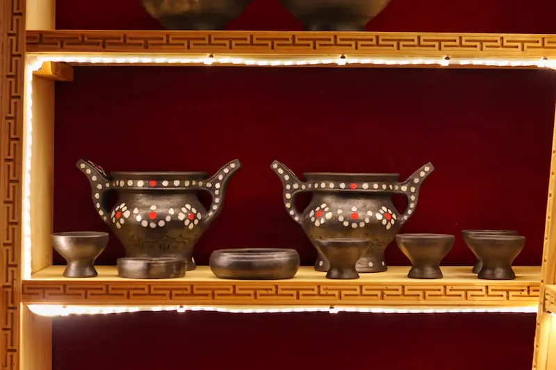 A Tibetan-style shelf displaying black pottery vessels and cups.