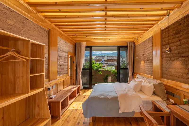 A clean and comfortable homestay room featuring natural wood furnishings and traditional mud walls.