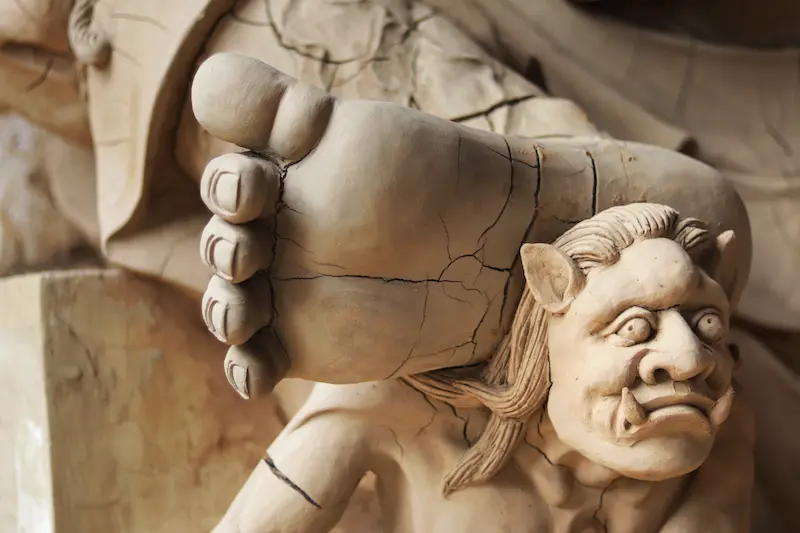 A close-up of a heavenly guardian standing over a mythical beast in a traditional sculpture.