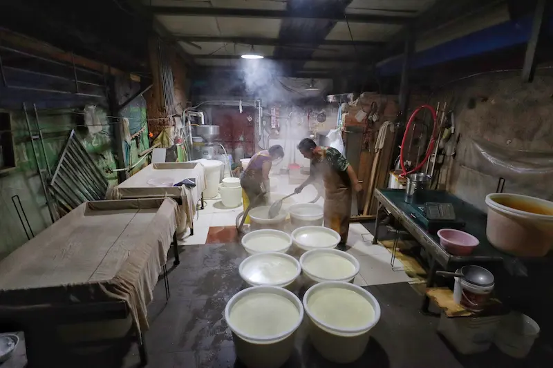 A couple transferring boiling soy milk into containers in an ancient tofu-making village.