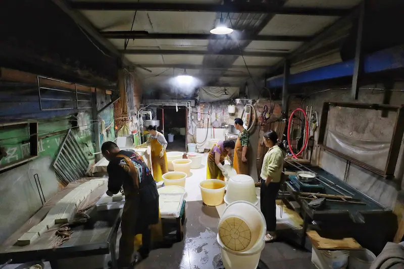 A family making tofu the traditional way inside an old mud house.