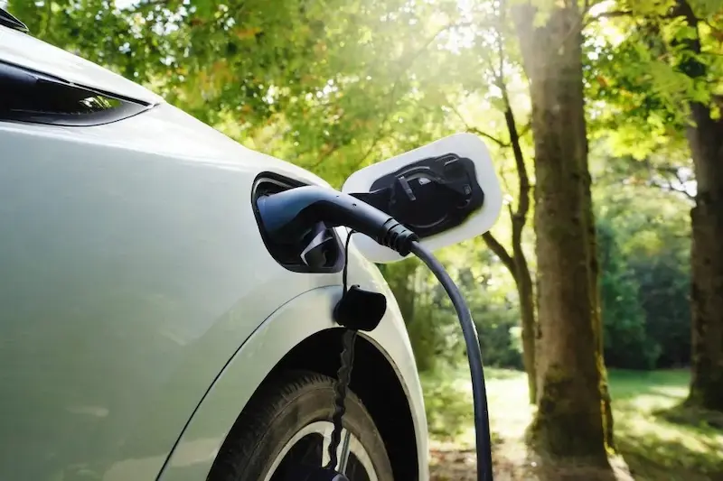 A white electric car charging with nature in the background.