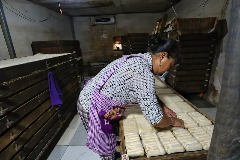 A woman flipping a sheet of nearly ready hairy tofu inside an old house.