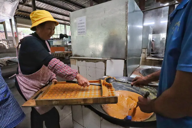 A woman smiling while making brown sugar using traditional methods.