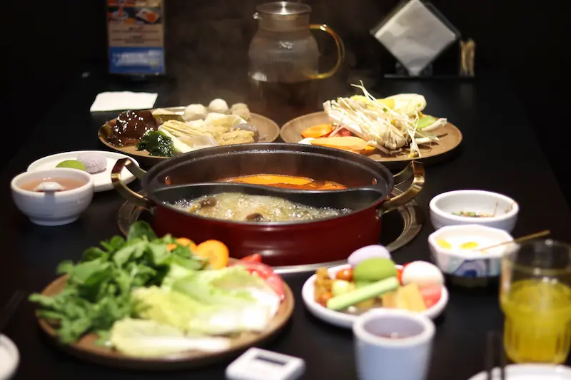 A yin-yang style wild mushroom hotpot with assorted ingredients arranged around it.