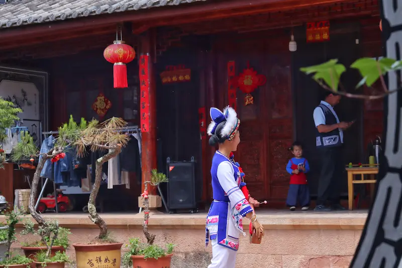 A young Bai mother dancing a traditional Bai dance with her daughter in the background.