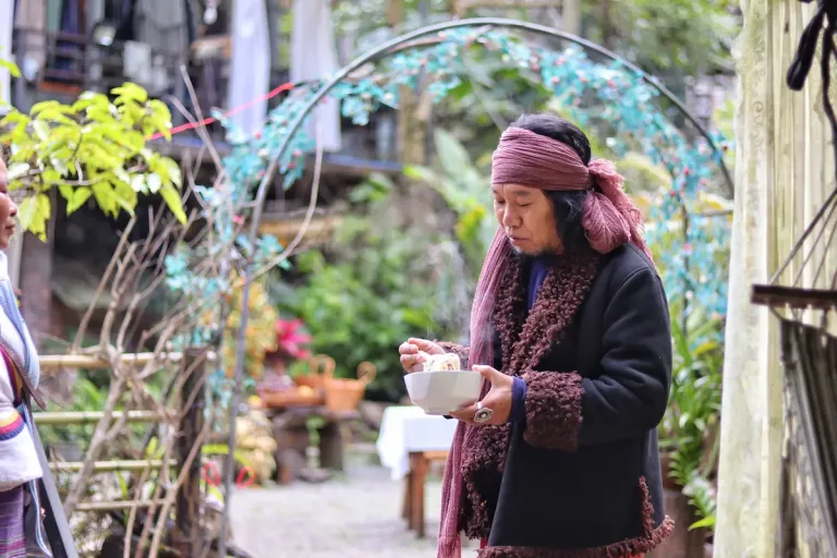An Akha man in Xishuangbanna standing and eating a bowl of noodles for breakfast.