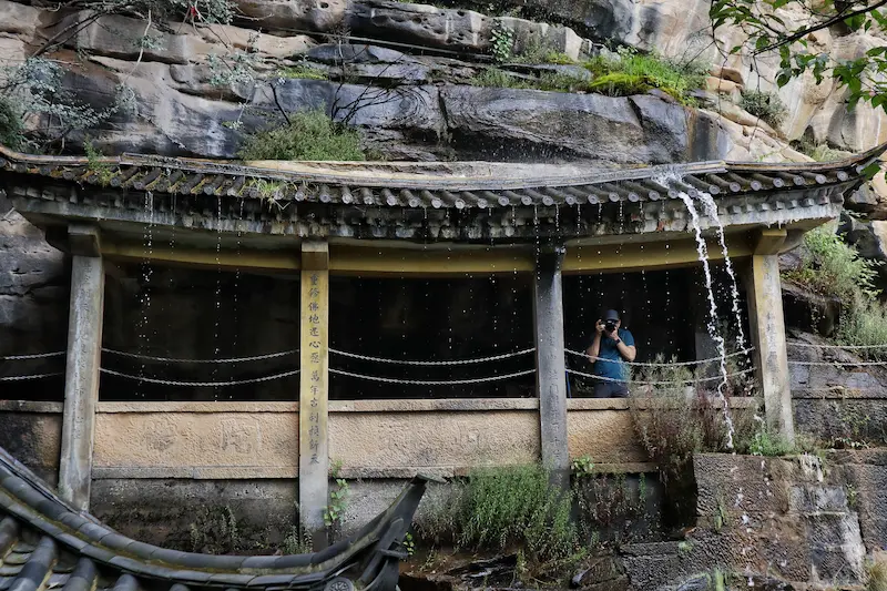 An American guest taking a photo from a cliffside pavilion with spring water dripping from the roof.