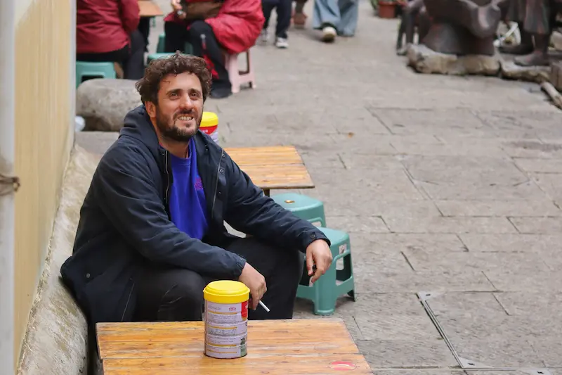 An Italian guest sitting at a small wooden table in a narrow alley in a quiet ancient town in Yunnan.