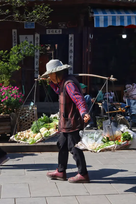 An elderly woman carrying local produce with a bamboo shoulder pole.