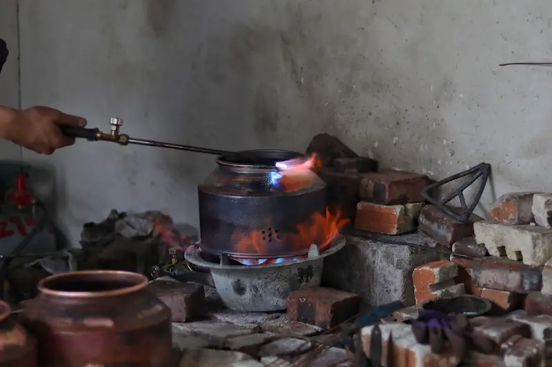 Artisan torch-firing a copper pot during traditional copperware making in Heqing, Dali, Yunnan.