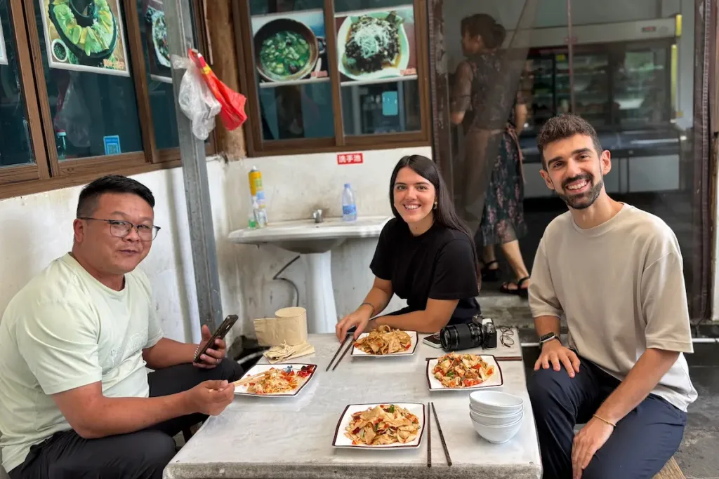 Baoshan driver Zhao smiling and enjoying a meal with two Italian guests.