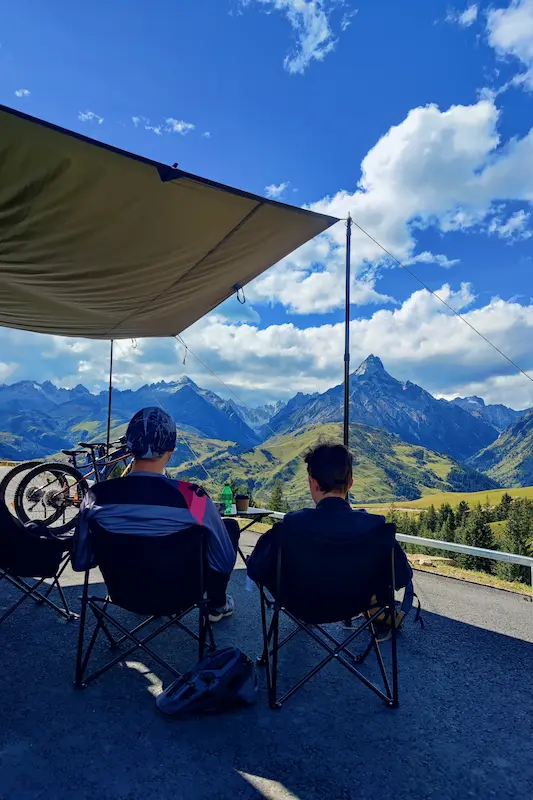 Cyclists resting under a shade canopy overlooking mountain valleys near Lijiang, Yunnan.