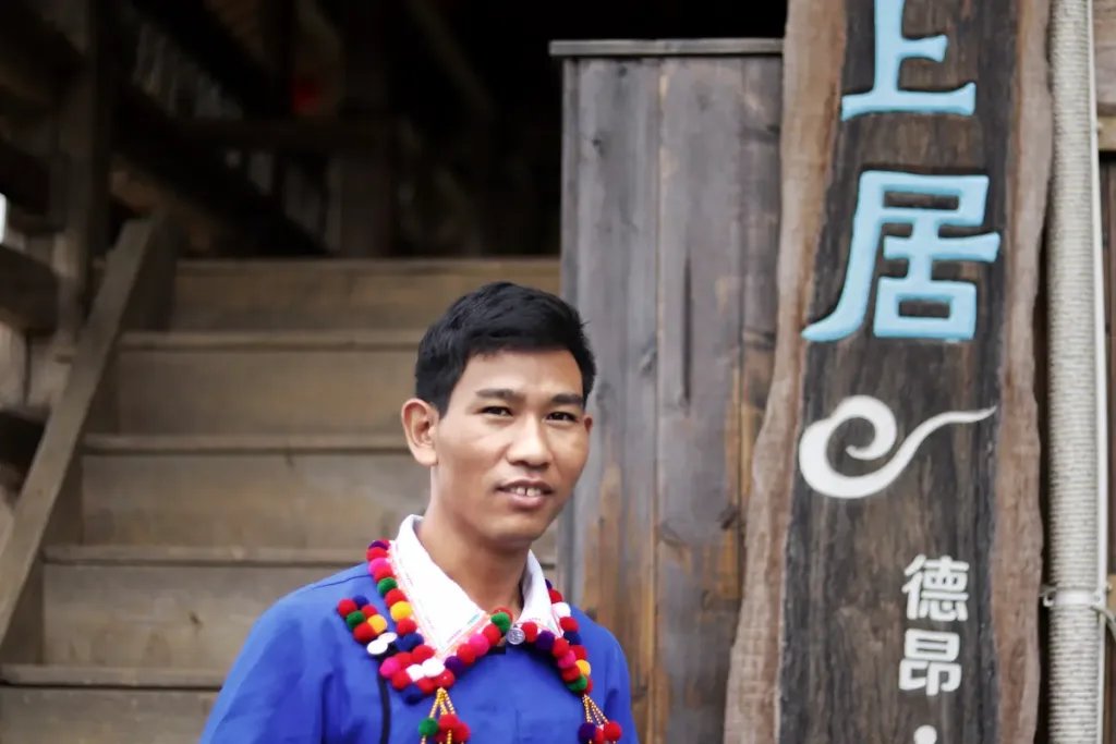 De'ang host Zhao dressed in traditional clothing smiling at the camera.