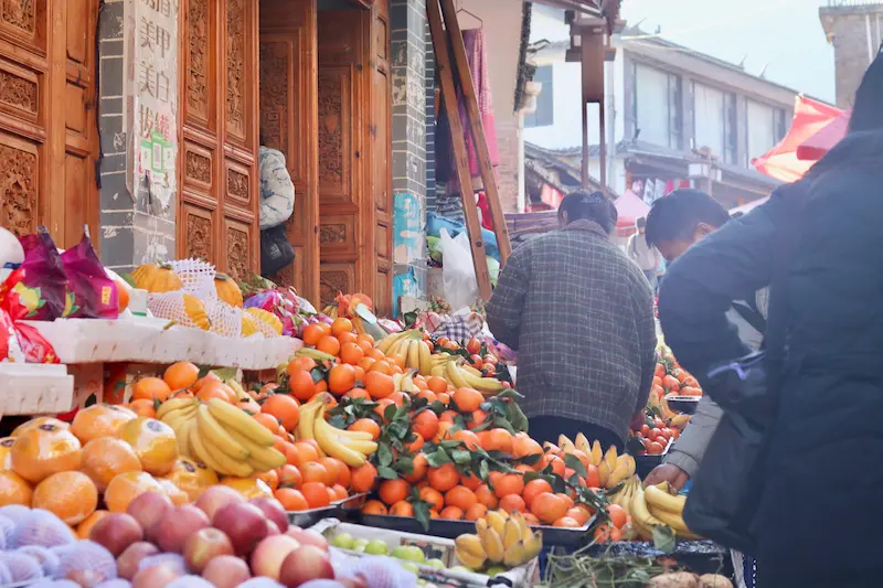 Fresh fruit stalls piled with oranges, bananas, and apples at a local market in Lijiang, Yunnan.