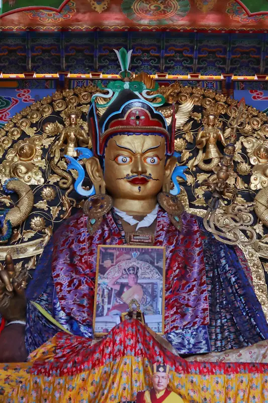 Gold statue of a Tibetan Buddhist deity with ornate crown and colorful robes inside a Yunnan monastery.