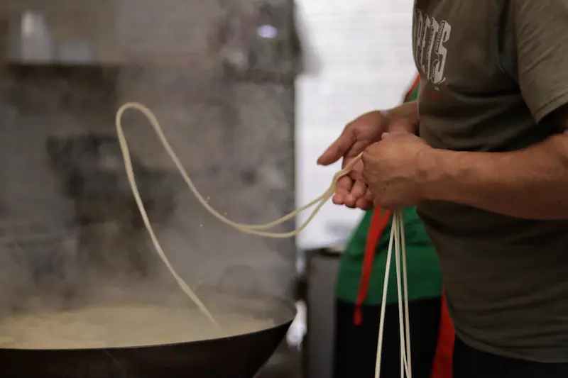Hand-pulling traditional one-strand noodles over a boiling wok in Weishan, Yunnan.