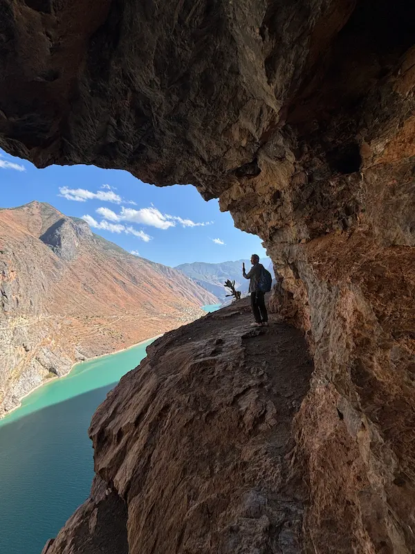 Hiker standing in a rock cave overlooking the turquoise Jinsha River valley near Stone Village, Lijiang, Yunnan