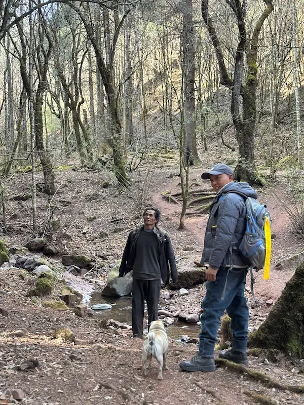 Hikers with a Lisu guide and dog crossing a stream in primary forest near a Lisu village outside Lijiang, Yunnan.