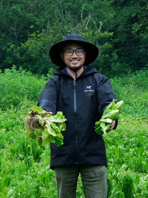 A portrait of Yunnan Eco Tours founder Leo standing in a vegetable garden, holding freshly harvested greens in his hands.