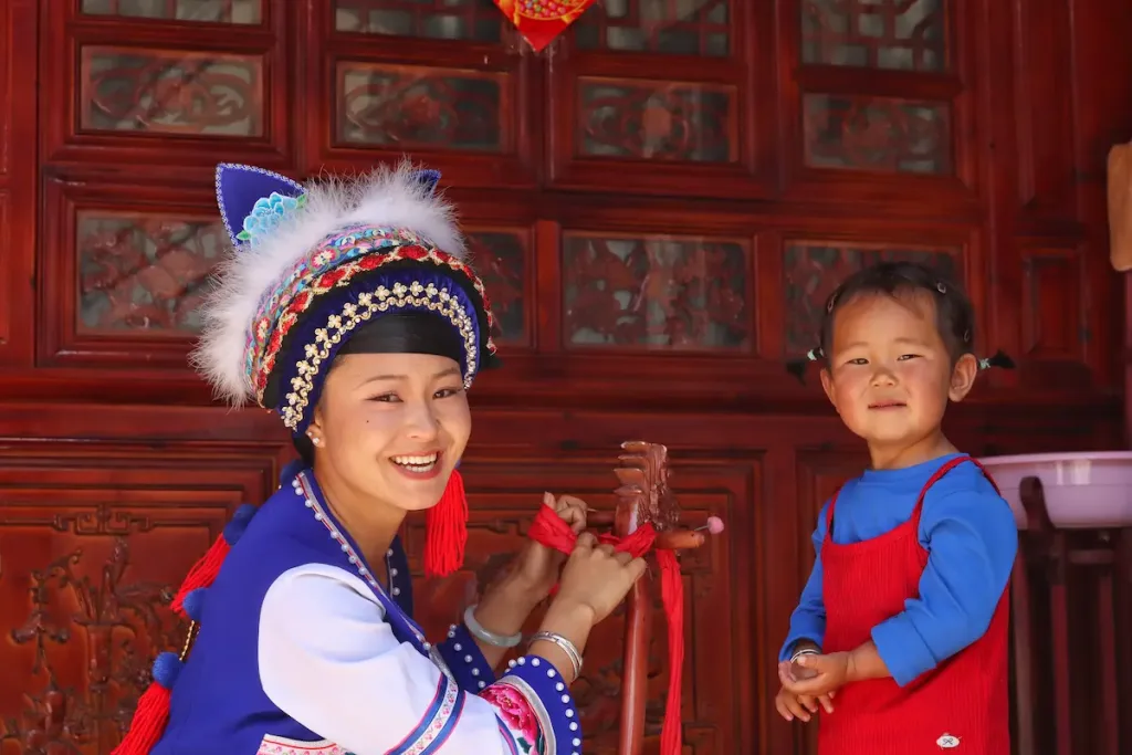A Bai woman in traditional clothing and her daughter smiling at the camera.