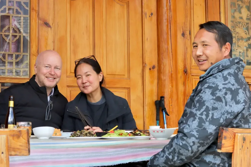 Lijiang driver Zhu smiling and enjoying a meal with two guests.