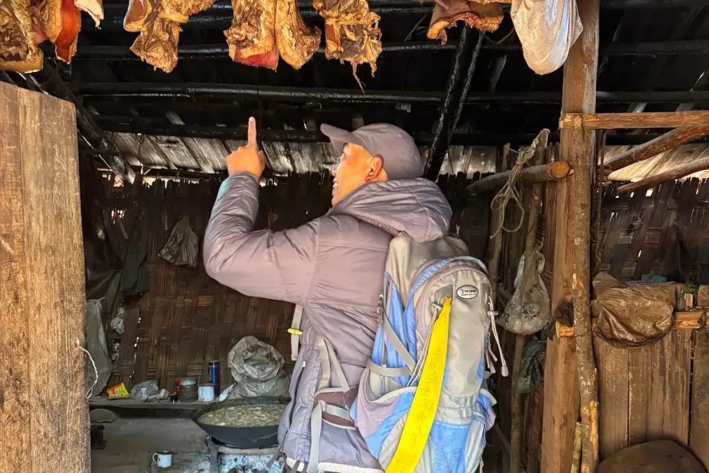 Lisu guide Chu in Lijiang pointing at dried food inside a traditional wooden house.