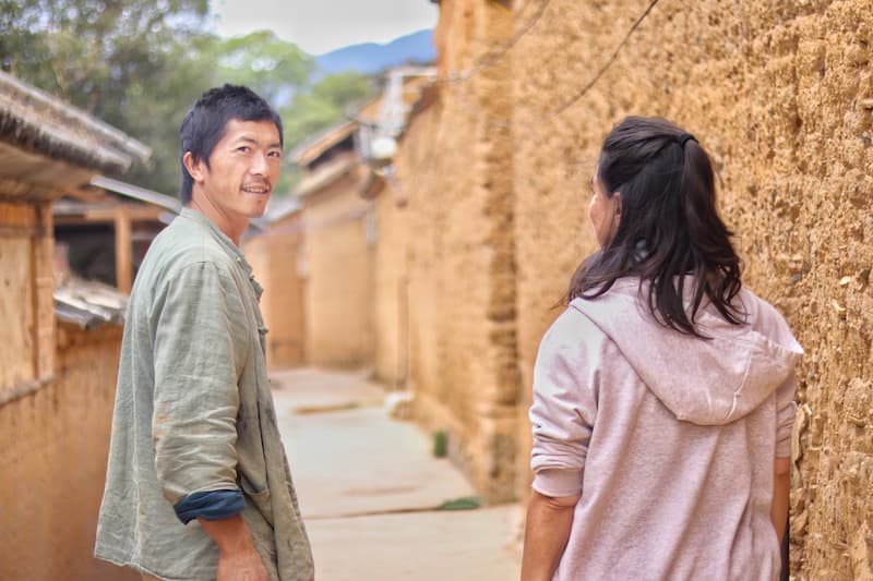 Local guide leading a visitor through narrow earthen-walled streets in Jingtian Village, Dali, Yunnan