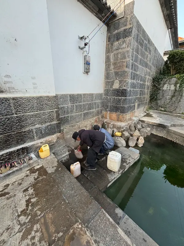 Locals collecting hot spring water from a natural spring using white plastic containers.
