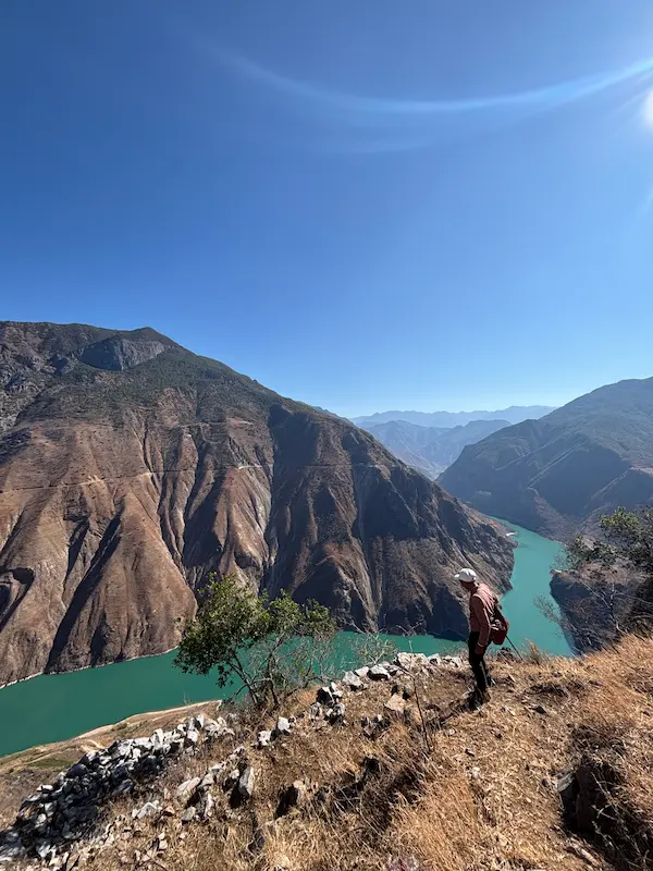 Naxi guide standing on a ridge overlooking the turquoise Jinsha River canyon near Stone Village, Lijiang, Yunnan