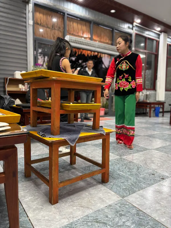 Stacked wooden stools used in a traditional 'jumping dishes' performance, with a Yi minority woman in colorful embroidered dress, Nanjian, Dali, Yunnan