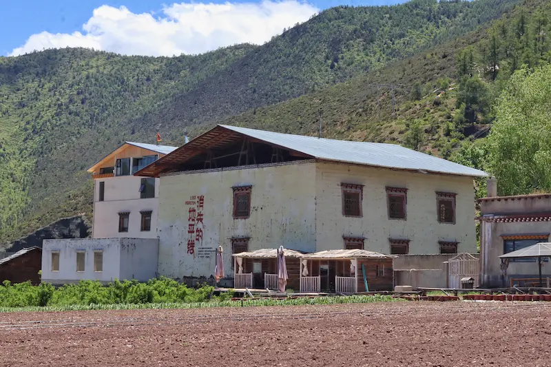 Traditional Tibetan-style farmhouse with painted windows and prayer flag, nestled in green mountains near Shangri-La.