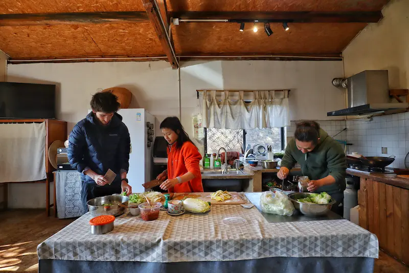 Two Australian guests cooking alongside a traditional soy sauce artisan in his kitchen.