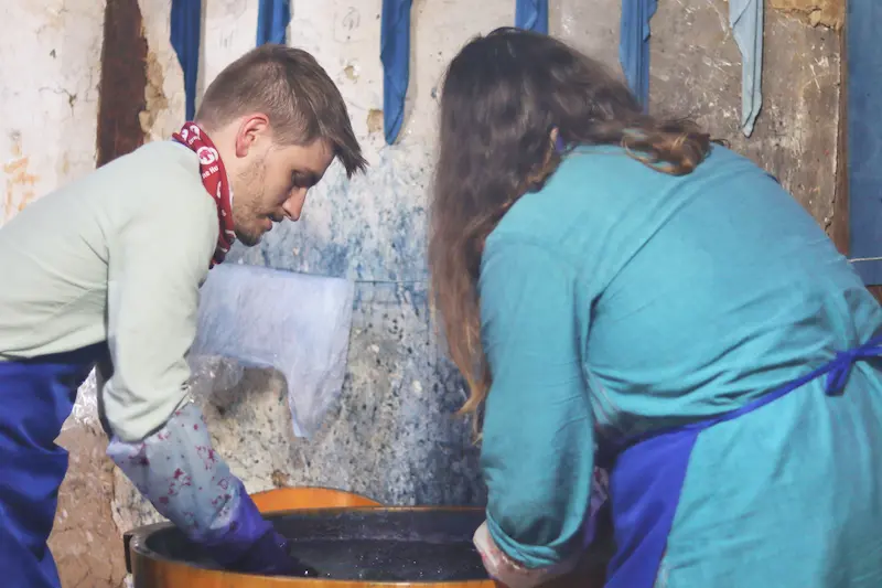 Two British guests dyeing their handmade items in a large container of dye.