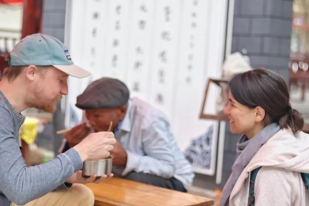 Two German guests trying a local snack at a market in Yunnan using a reusable bowl.