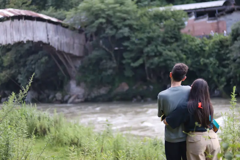 Two Italian guests embracing while enjoying the view of an ancient wooden bridge in Yunnan.