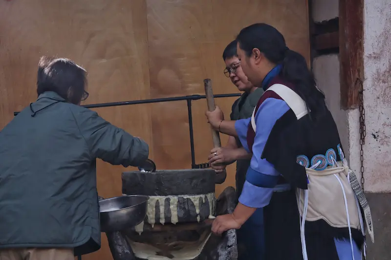 Two Singaporean guests grinding Lijiang chicken pea using a traditional stone mill.